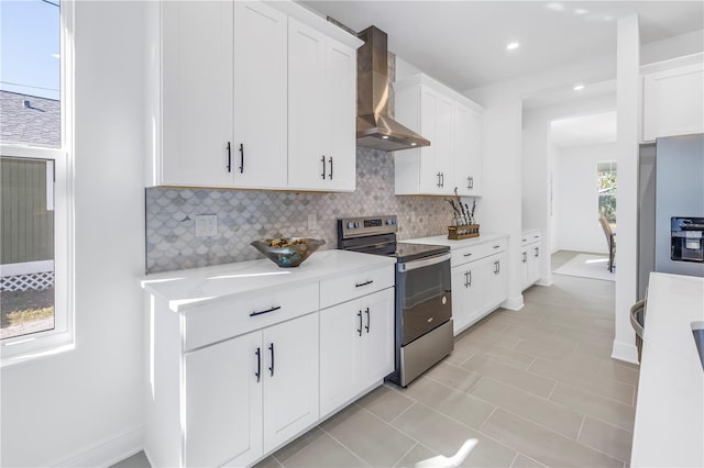 kitchen featuring backsplash, wall chimney exhaust hood, light tile patterned floors, white cabinetry, and stainless steel range with electric cooktop