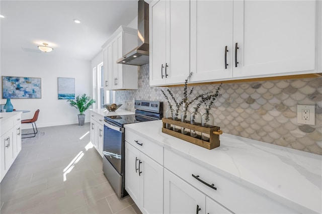 kitchen with decorative backsplash, light stone countertops, wall chimney range hood, electric stove, and white cabinets