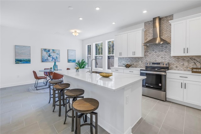 kitchen with white cabinetry, stainless steel electric range oven, wall chimney exhaust hood, and a kitchen island with sink