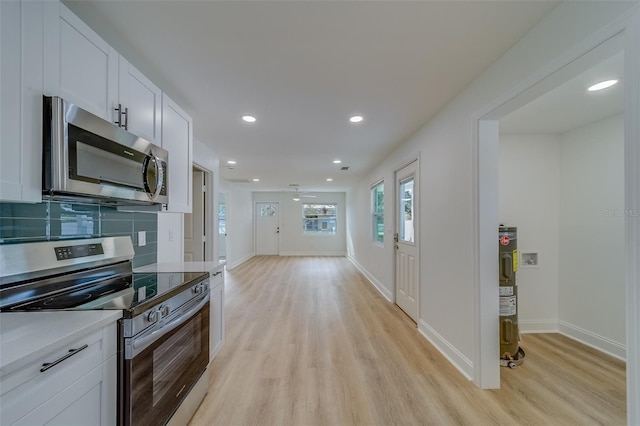 kitchen featuring appliances with stainless steel finishes, white cabinetry, decorative backsplash, light hardwood / wood-style floors, and electric water heater