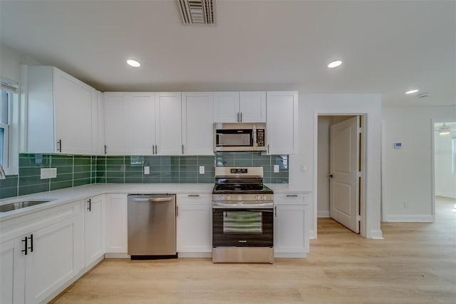 kitchen with appliances with stainless steel finishes, white cabinetry, sink, backsplash, and light wood-type flooring