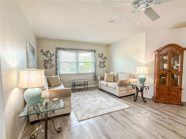 living room featuring ceiling fan, a textured ceiling, and light hardwood / wood-style floors