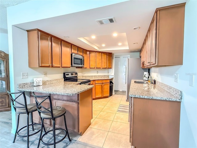 kitchen with appliances with stainless steel finishes, a breakfast bar area, kitchen peninsula, a raised ceiling, and light stone countertops