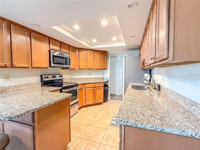 kitchen with light stone counters, sink, stainless steel appliances, and a raised ceiling