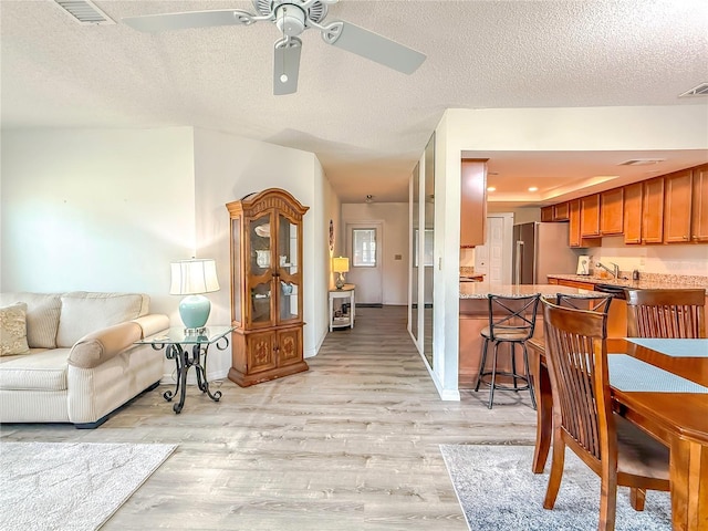 living room featuring ceiling fan, sink, light hardwood / wood-style floors, and a textured ceiling