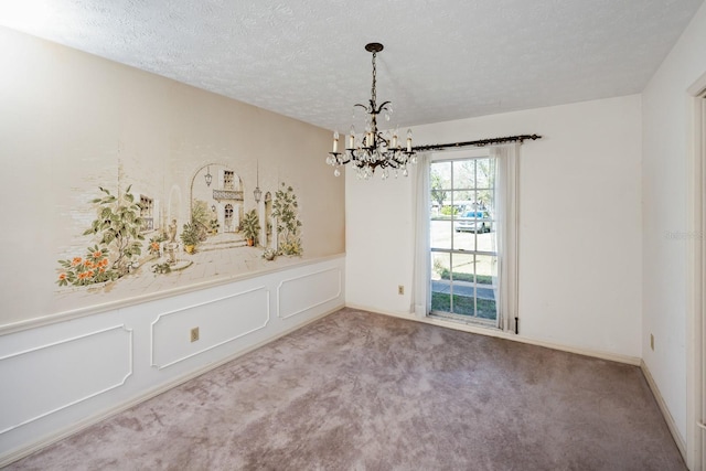 spare room featuring carpet, a textured ceiling, and a notable chandelier