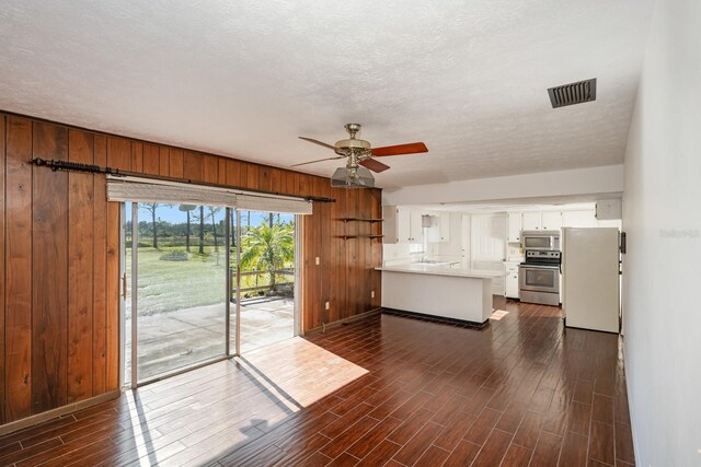 unfurnished living room featuring a textured ceiling, dark wood-type flooring, ceiling fan, and wooden walls