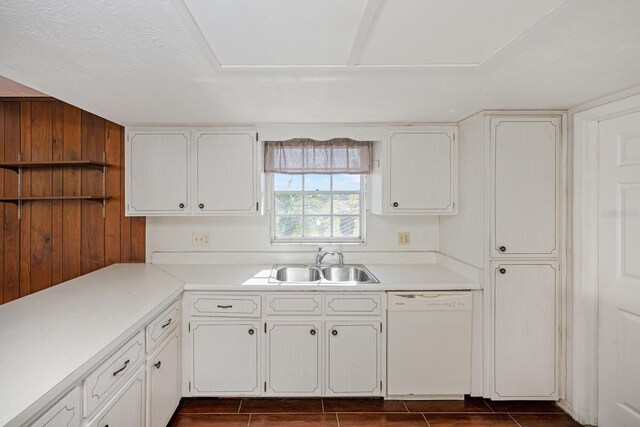 kitchen featuring wood walls, dishwasher, white cabinets, and sink