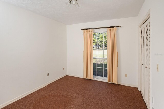 unfurnished room with a textured ceiling and dark carpet