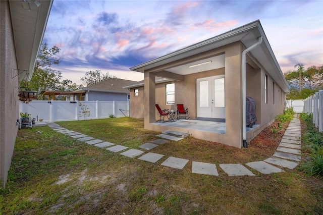 back house at dusk featuring a yard and a patio