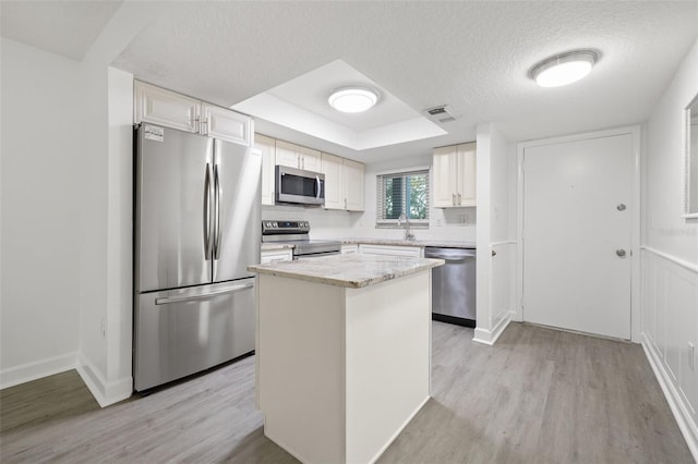 kitchen featuring sink, stainless steel appliances, a raised ceiling, white cabinets, and light wood-type flooring