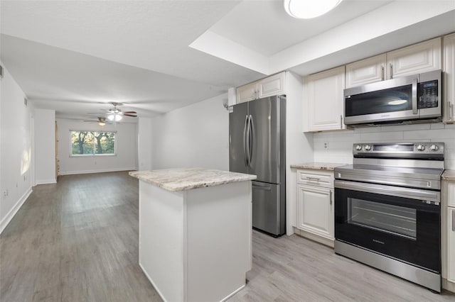 kitchen featuring backsplash, light hardwood / wood-style flooring, ceiling fan, light stone countertops, and appliances with stainless steel finishes