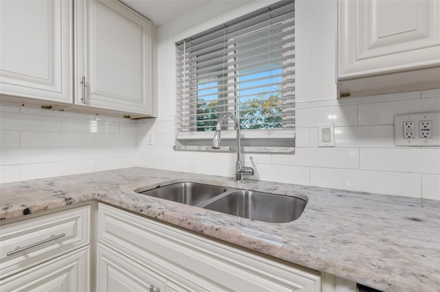 kitchen with light stone counters, white cabinetry, and sink