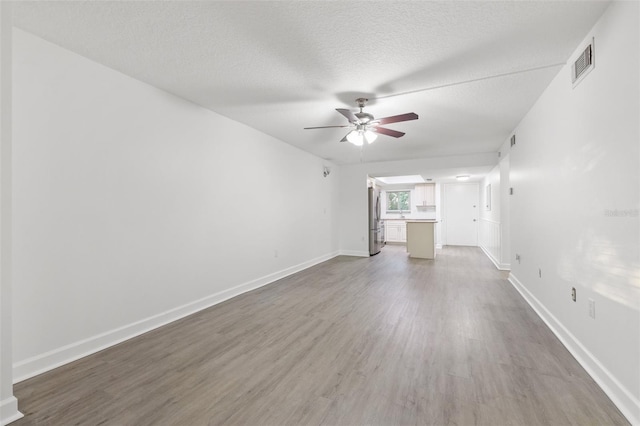 unfurnished living room featuring hardwood / wood-style flooring, ceiling fan, and a textured ceiling