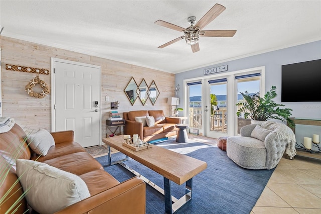 tiled living room featuring wood walls, french doors, crown molding, ceiling fan, and a textured ceiling