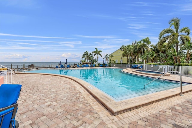 view of swimming pool featuring a water view, a patio, and a hot tub