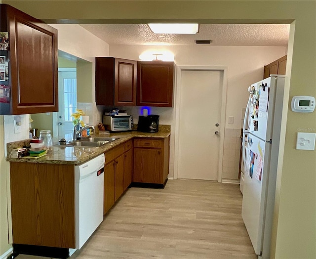 kitchen featuring light stone countertops, sink, light hardwood / wood-style flooring, a textured ceiling, and white appliances