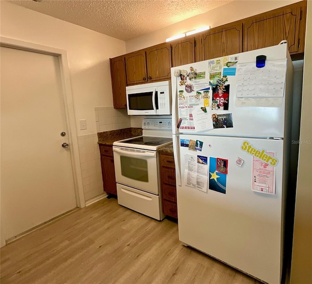 kitchen featuring light wood-type flooring, a textured ceiling, white appliances, and backsplash