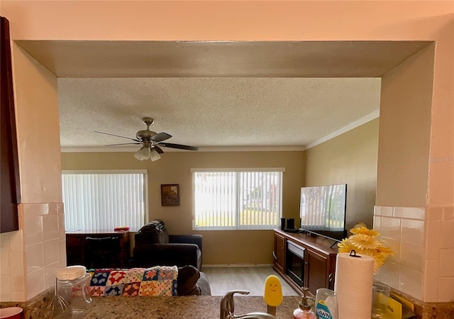 living room with ceiling fan, crown molding, and a textured ceiling