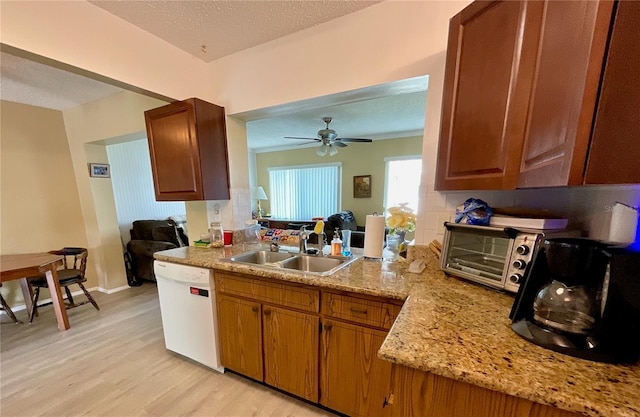 kitchen with light stone countertops, dishwasher, sink, light hardwood / wood-style floors, and a textured ceiling