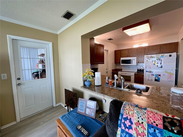 kitchen with a textured ceiling, sink, white appliances, and light hardwood / wood-style flooring