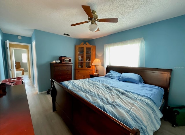 bedroom with ceiling fan, light hardwood / wood-style flooring, and a textured ceiling