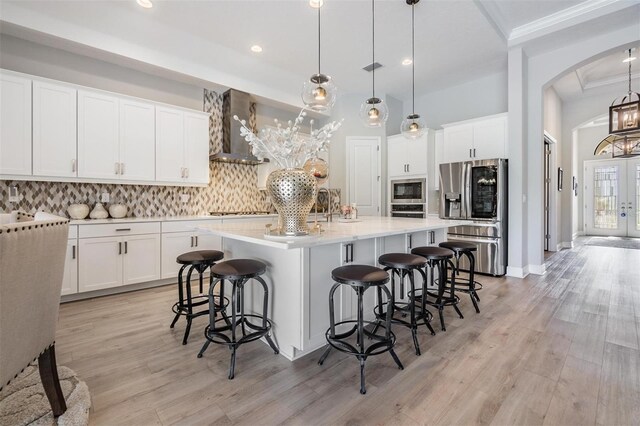 kitchen featuring a spacious island, wall chimney range hood, stainless steel refrigerator with ice dispenser, and hanging light fixtures