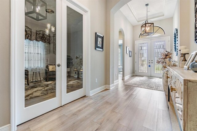 foyer with light wood-type flooring, a tray ceiling, and french doors