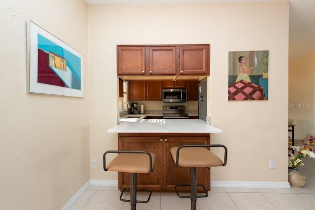 kitchen featuring a kitchen breakfast bar, sink, light tile patterned floors, and stainless steel appliances