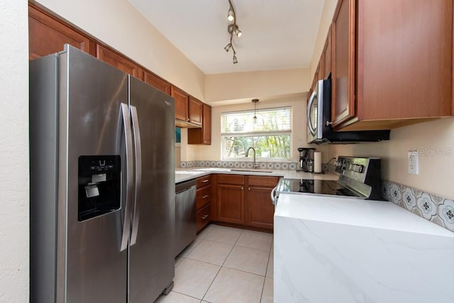 kitchen featuring light stone countertops, stainless steel appliances, sink, light tile patterned floors, and decorative light fixtures