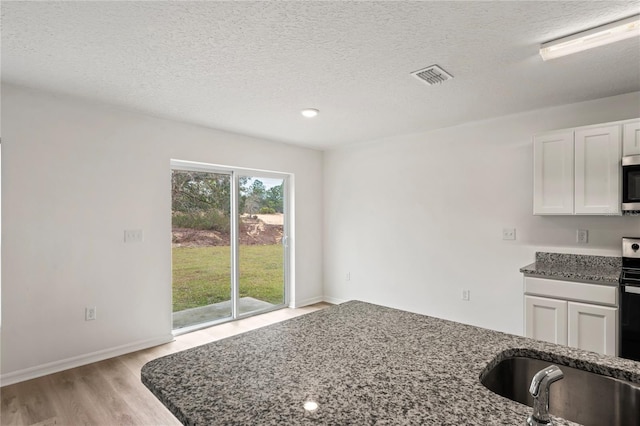 kitchen with white cabinets, dark stone countertops, light wood-type flooring, a textured ceiling, and appliances with stainless steel finishes