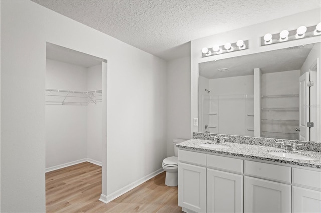 bathroom featuring walk in shower, a textured ceiling, toilet, vanity, and hardwood / wood-style flooring