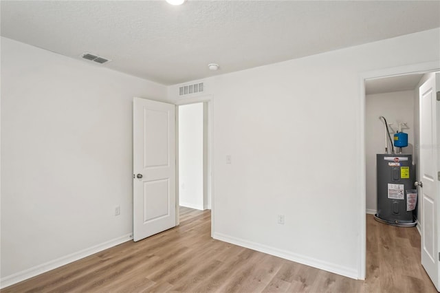 unfurnished room featuring a textured ceiling, light wood-type flooring, and water heater