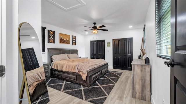 bedroom with two closets, hardwood / wood-style floors, and ceiling fan