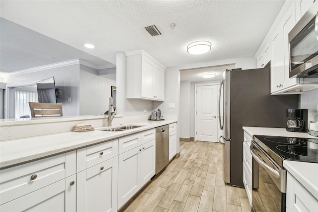 kitchen with white cabinets, sink, ornamental molding, a textured ceiling, and appliances with stainless steel finishes