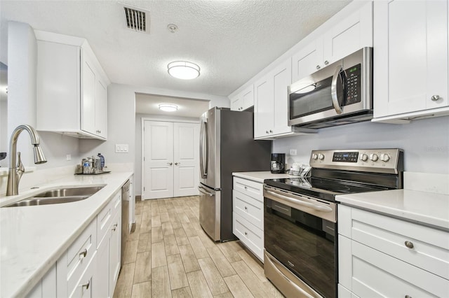 kitchen with sink, a textured ceiling, light hardwood / wood-style floors, white cabinetry, and stainless steel appliances