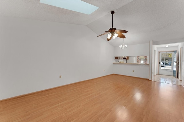 unfurnished living room featuring a textured ceiling, vaulted ceiling with skylight, ceiling fan with notable chandelier, and light hardwood / wood-style flooring