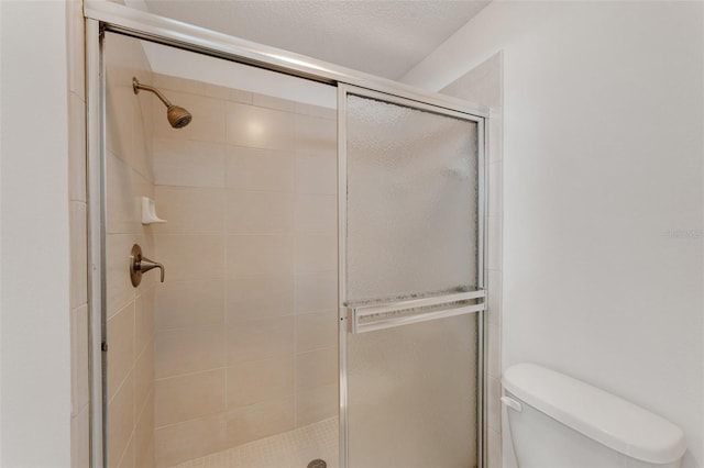 bathroom with toilet, a shower with shower door, and a textured ceiling