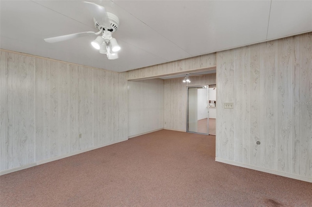 carpeted empty room with ceiling fan and wood walls