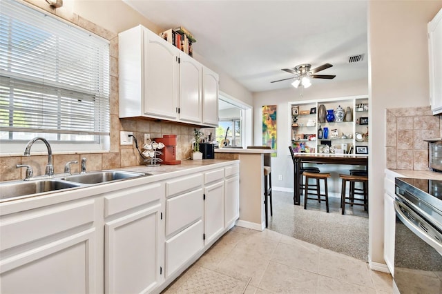 kitchen featuring tasteful backsplash, sink, white cabinets, light tile patterned floors, and stainless steel range oven