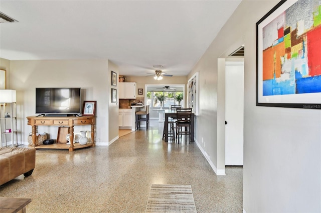 living area with ceiling fan, speckled floor, visible vents, and baseboards