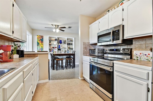 kitchen featuring appliances with stainless steel finishes, decorative backsplash, tile counters, and white cabinets