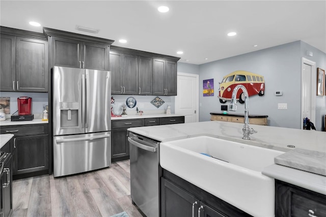 kitchen with light stone countertops, sink, stainless steel appliances, and light wood-type flooring