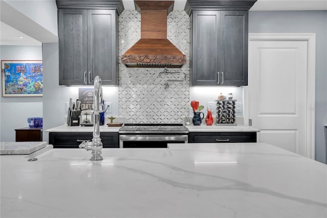 kitchen featuring light stone countertops, dark brown cabinetry, gas stove, decorative backsplash, and premium range hood