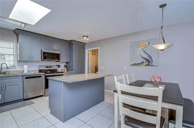 kitchen with appliances with stainless steel finishes, a skylight, sink, a center island, and hanging light fixtures