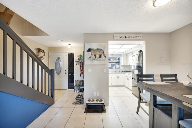 kitchen with black fridge, white cabinetry, a textured ceiling, and light tile patterned floors