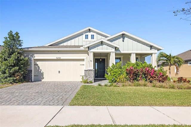 craftsman house with a front lawn, board and batten siding, decorative driveway, and an attached garage