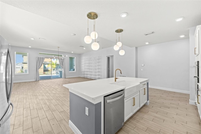 kitchen featuring white cabinetry, sink, stainless steel appliances, pendant lighting, and a kitchen island with sink