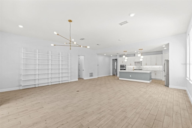 unfurnished living room featuring a chandelier and light hardwood / wood-style floors