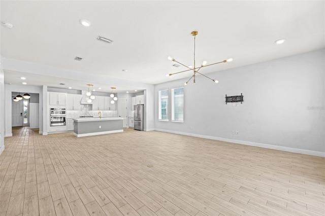 unfurnished living room with a chandelier, sink, and light hardwood / wood-style floors